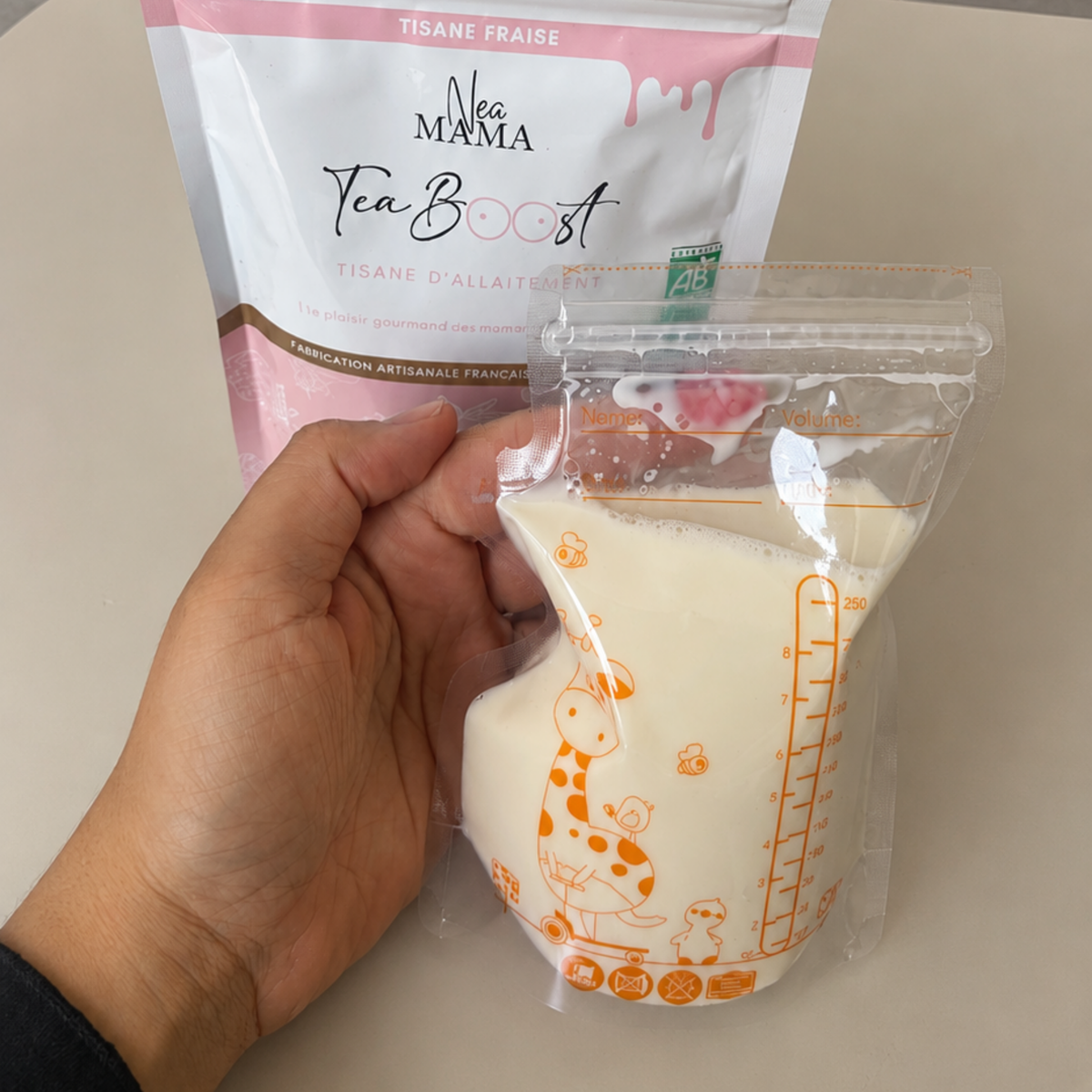Sachet de conservation de lait maternel rempli de lait tiré, tenu à la main devant un sachet de tisane d'allaitement NEA MAMA