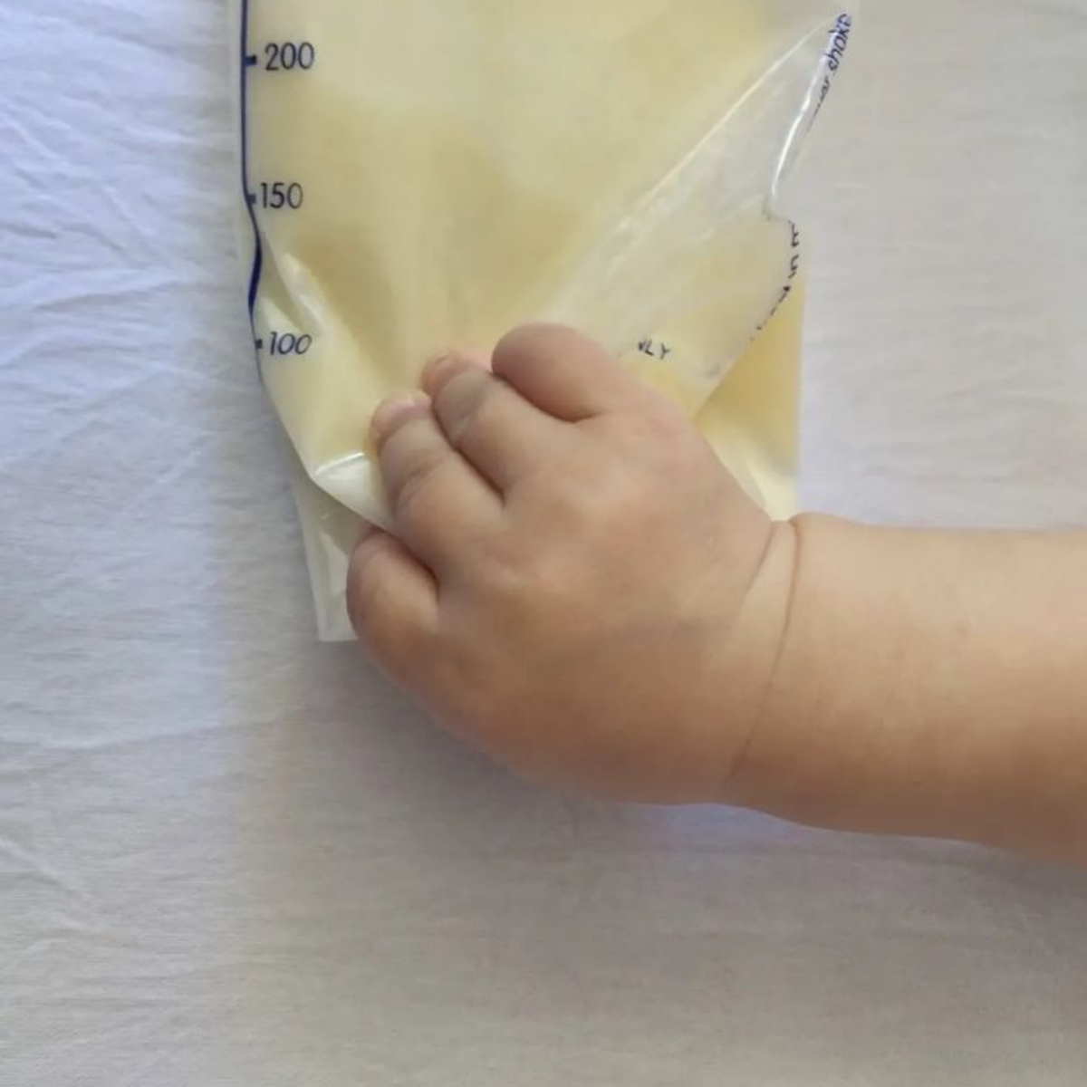 Main de bébé posée sur un sachet de lait maternel